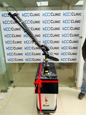 Wheel-mounted medical hoist with an adjustable boom and handle, secured with red straps in a clinic hallway.