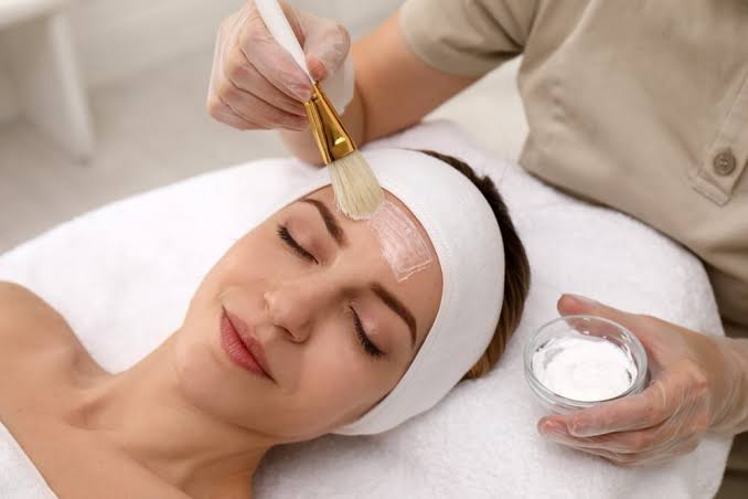 Relaxed woman receives a facial as a professional brushes a cream mask onto her forehead on a spa table